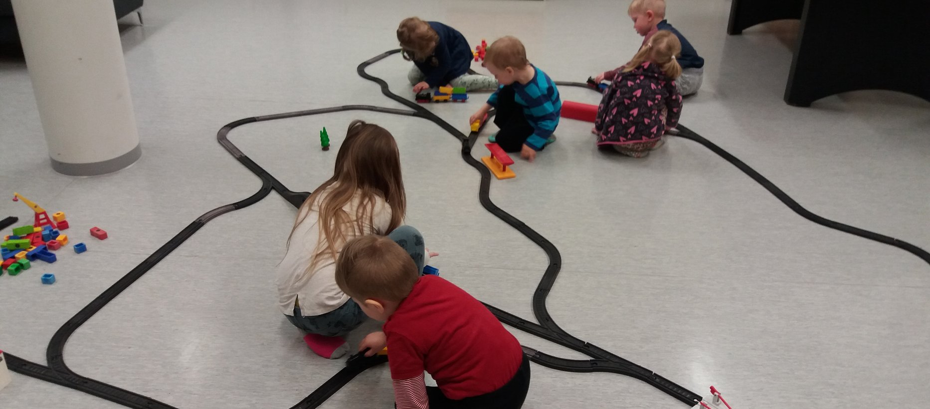 Lapset leikkivät lattialla muovisella junaradalla.