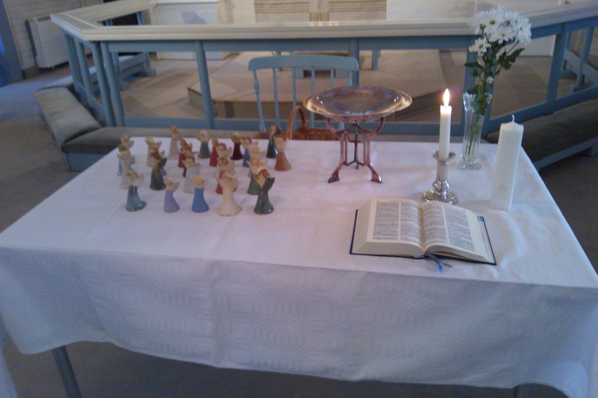 Kasteen sunnuntai. Pöydällä valkoisen liinan päällä enkelit kastetuille, kastemalja,kynttilä,kukat ja raamattu