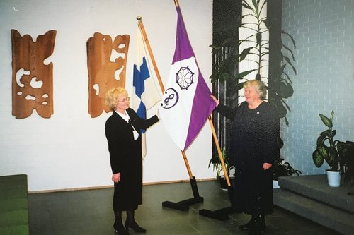 Vilppulan kirkkokuoron lippu ja Suomen lippu. Kaksi naista kuorosta esittelevät Vilppulan kirkkokuoron lippua.